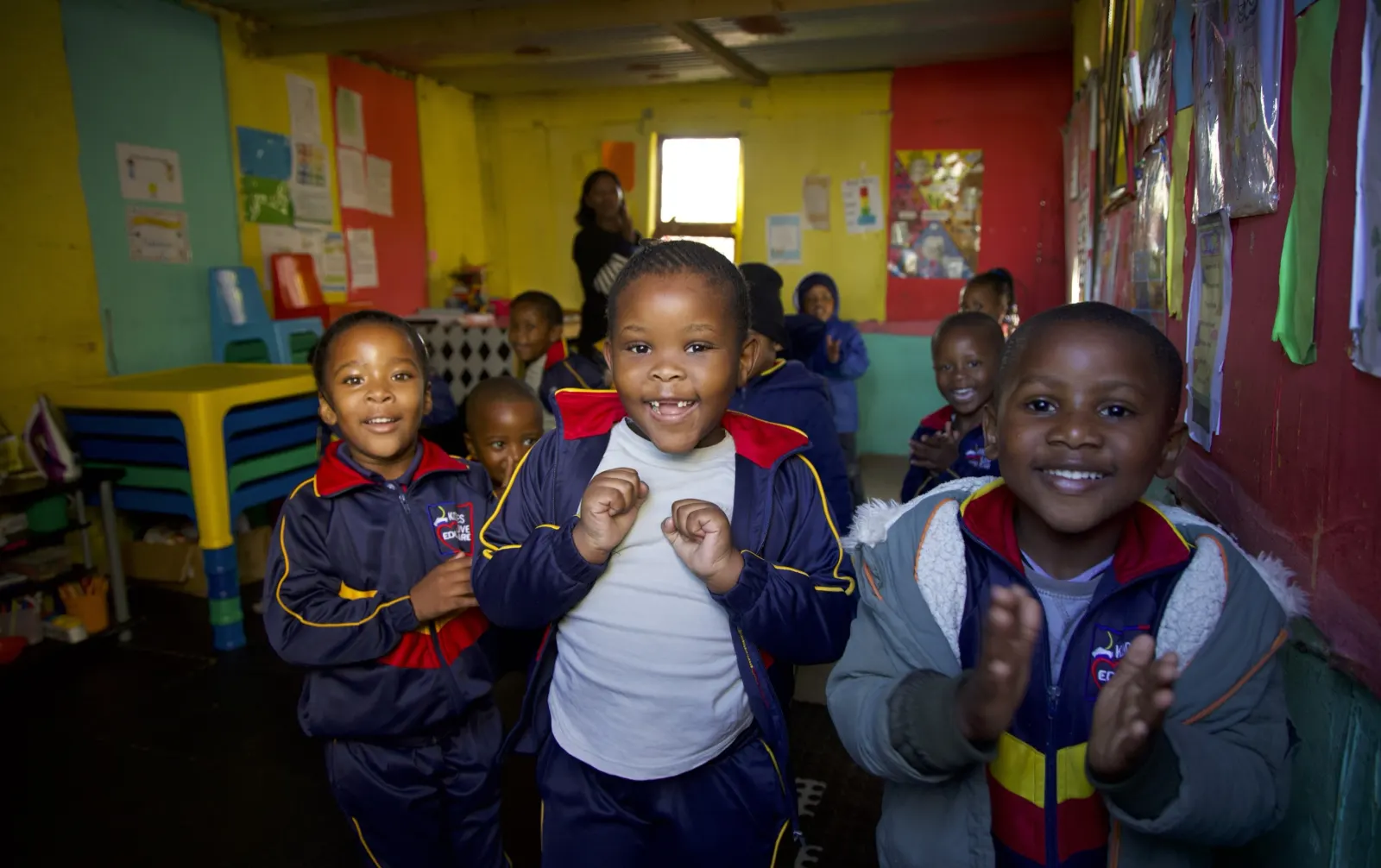 Smiling children in school jerseys clap their hands in a classroom.