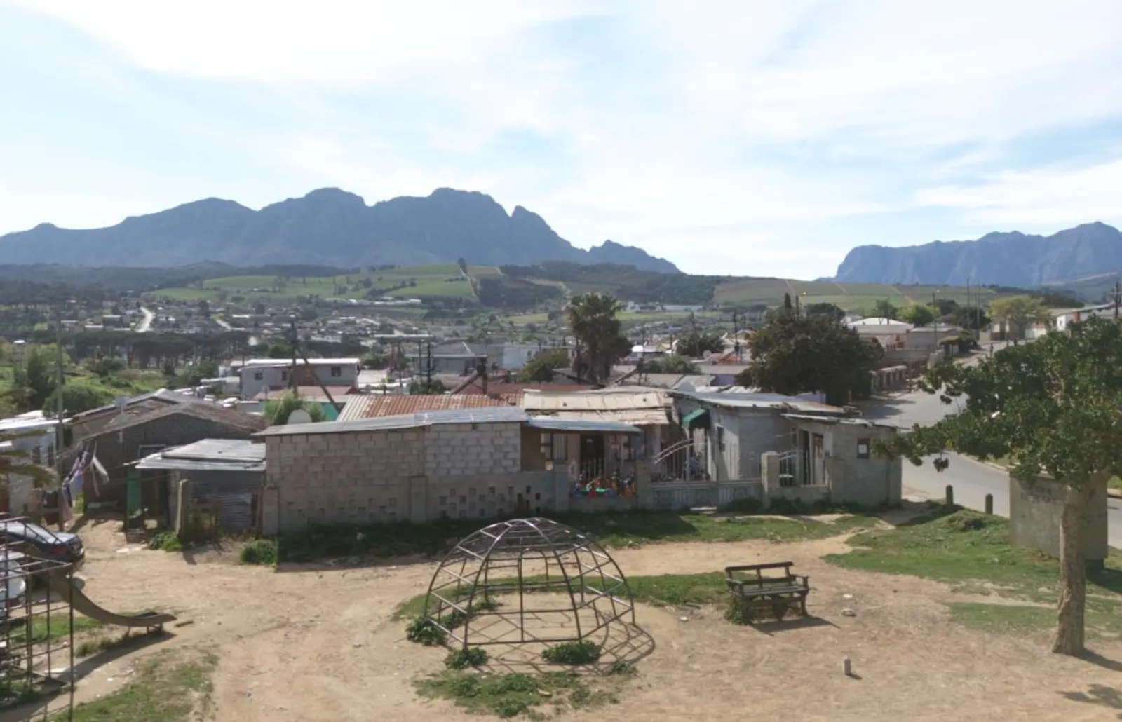 An aerial view of Kayamandi with homes, trees and a playground, with mountains behind.