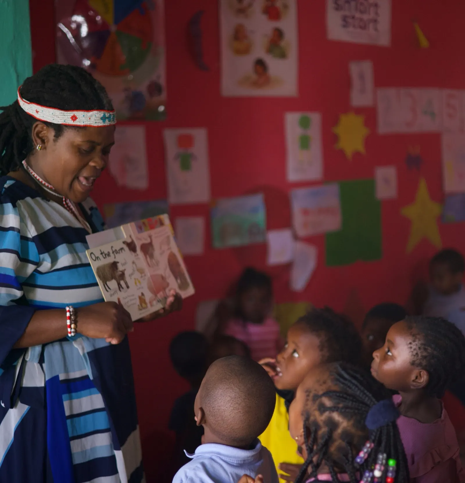 Andiswa Damane reads with young children in a classroom with a pink wall.