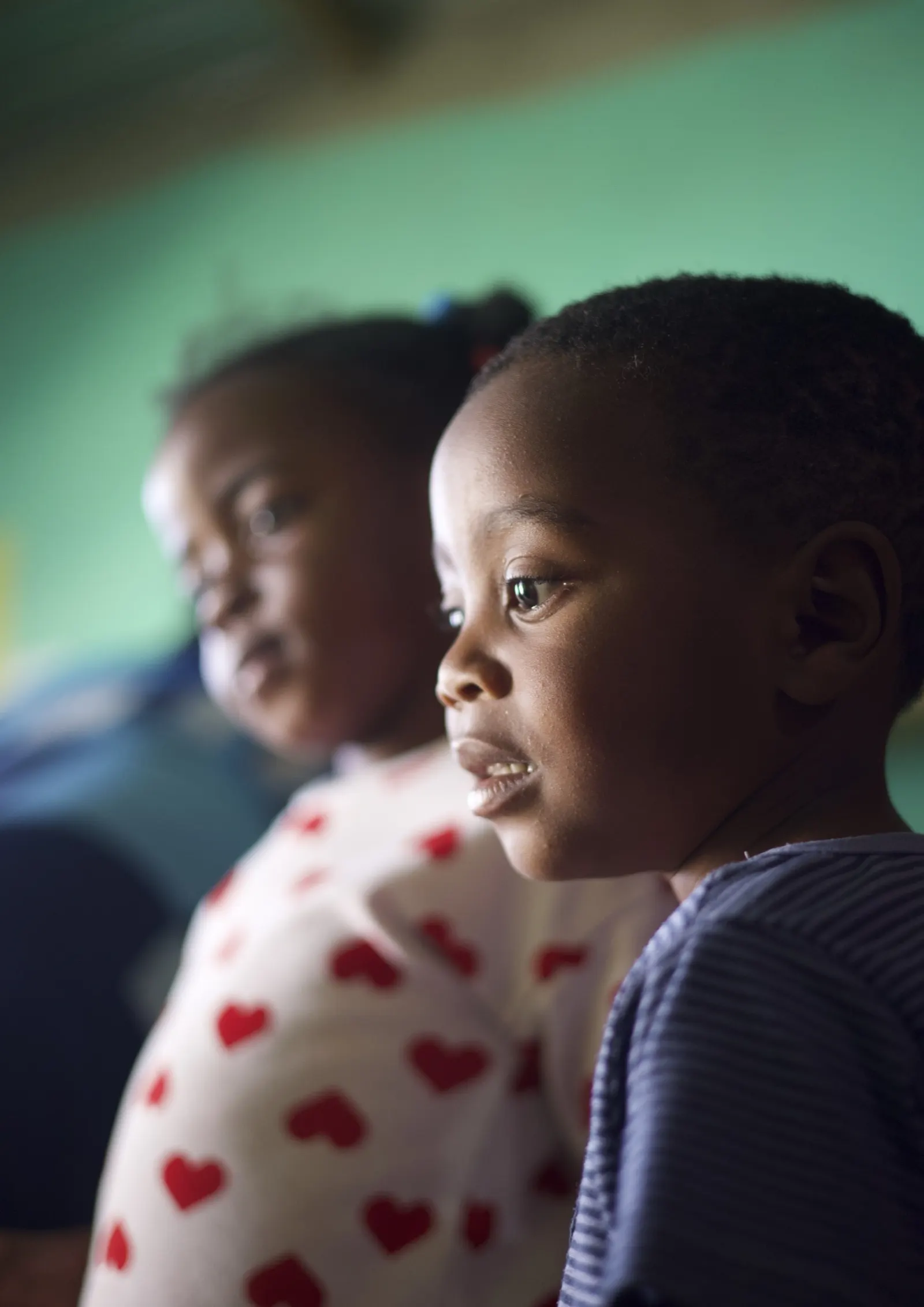 Two young children, one in a striped top and one in a heart-print top, look to the side.